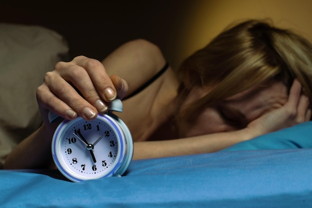 The woman cannot wake up in the morning Poor sleep violation of the regimen lack of sleep concept A middleaged woman turns off the alarm clock