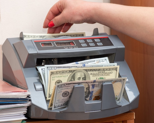 Woman cashier putting one hundred dollars american banknotes into currency counter at checkout counter