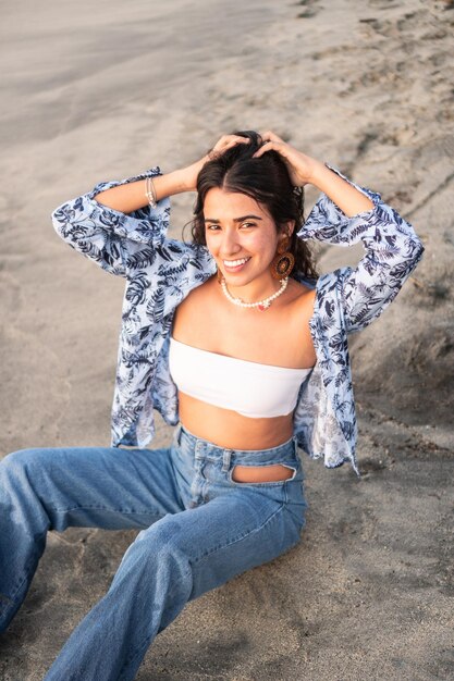 Woman in casual clothes sitting on the shore of the beach posing in front of the camera