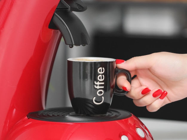 Woman caucasian hand with red manicure takes black mug with red coffee maker