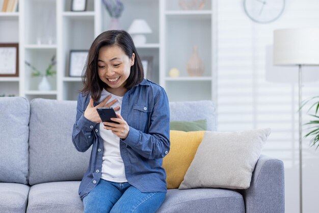 Woman celebrating victory at home looking at phone screen satisfied asian woman happy received