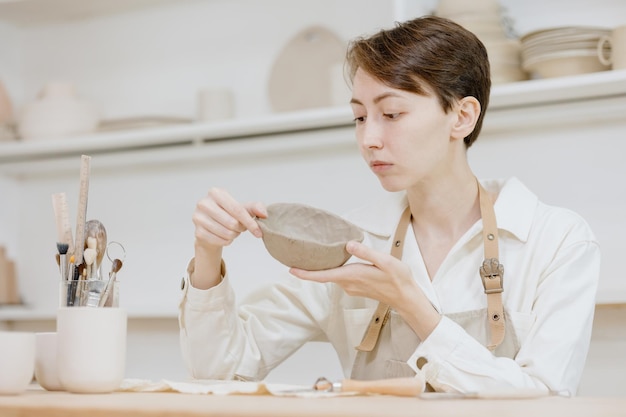 Woman ceramist in the workshop makes mugs out of clay small business or hobby is the creation of