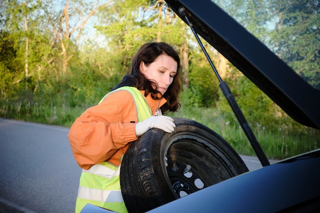 Woman changes the damaged wheel of the car