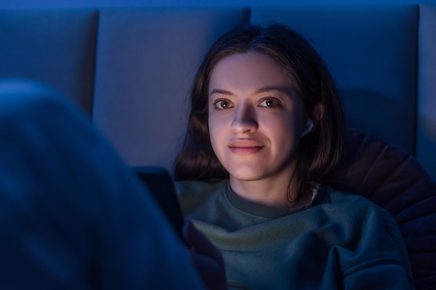 Woman chatting and surfing on internet with smartphone late at night lying on bed