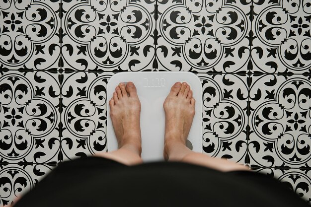 Photo woman checking her weight on weighing scales in bathroom