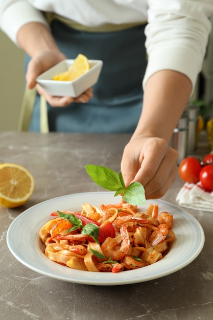 Woman chef putting basil on pasta with shrimps, close up