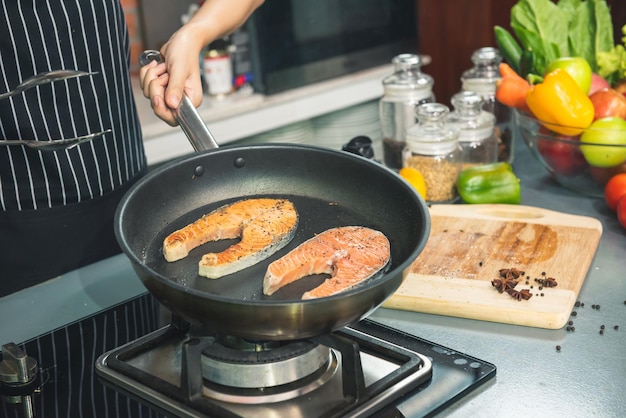 Woman chef salts raw salmon steak in a frying pan. Healthy seafood. Chef preparing salmon steak on stove. Cooking food concept.