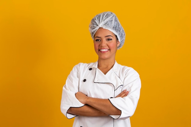 Woman chef wearing uniform and bonnet standing arms crossed and posing over isolated yellow background occupation concept