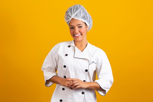 Woman chef wearing uniform and bonnet standing arms crossed and posing over isolated yellow background occupation concept