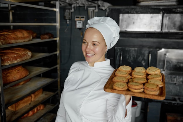 Woman chef with tray of appetite delicious pastry standing at bakery kitchen