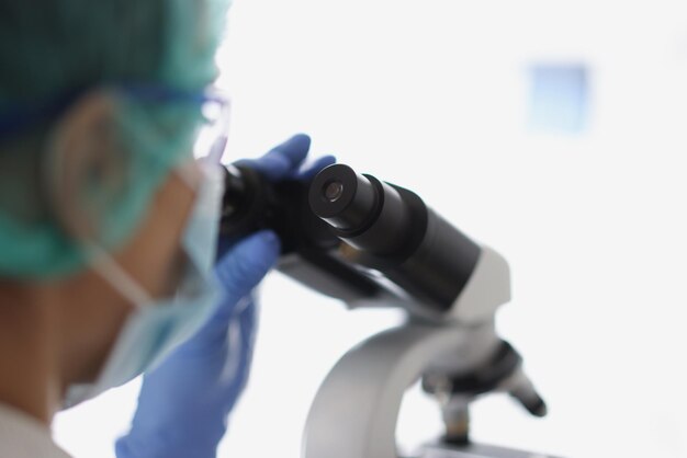 Woman chemist in blue protective glove look at microscope in chemistry lab