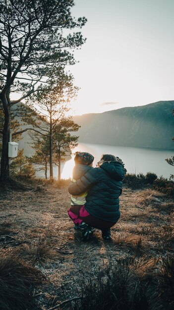 Photo a woman and a child are hugging in front of a lake.