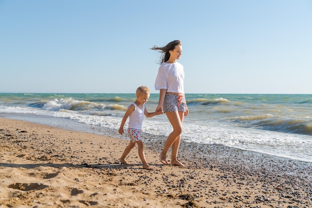 A woman and a child are walking on the beach.