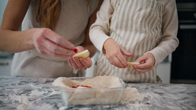 Woman child hands putting apple at baking form close up Family preparing pie