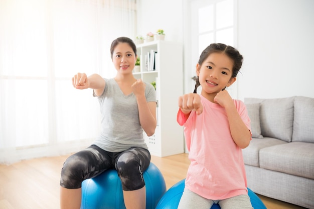 woman and children hands gesture as boxing and hit air with sitting on the fitness ball training balance and strength in the professional yoga class at gym center.