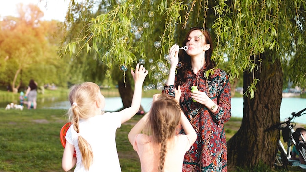 Woman and children play with soap balloons. Romantic portrait of young woman with soap balloons. Sunny Valley on a summer day