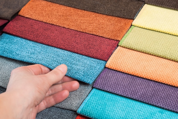 Woman chooses samples of colored fabric on table close up