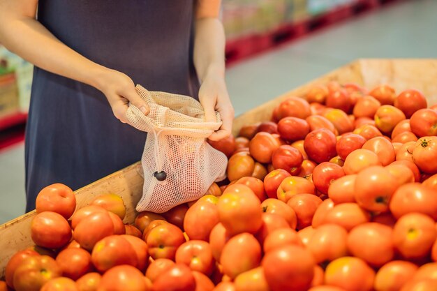 A woman chooses tomatoes in a supermarket without using a plastic bag reusable bag for buying