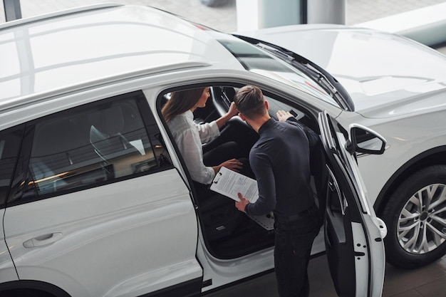 Woman choosing car by help of male assistant indoors in the salon.