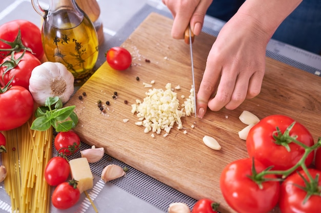 Woman chopping garlic on wooden cutting board at domestic kitchen