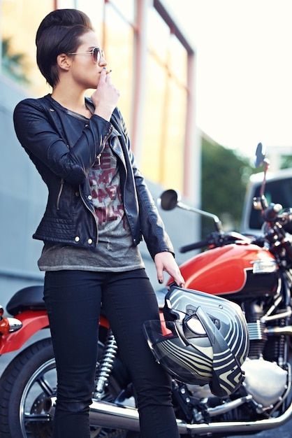 Photo woman city and motorcycle while smoking on a break from her journey or commute in italy punk style tobacco and woman with a nicotine cigarette in milan on motorbike with urban and edgy fashion