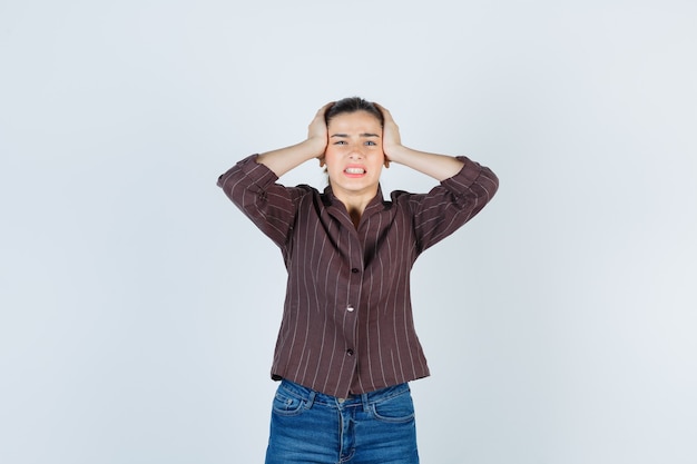 woman clasping head with hands in shirt, jeans and looking irritated. front view.