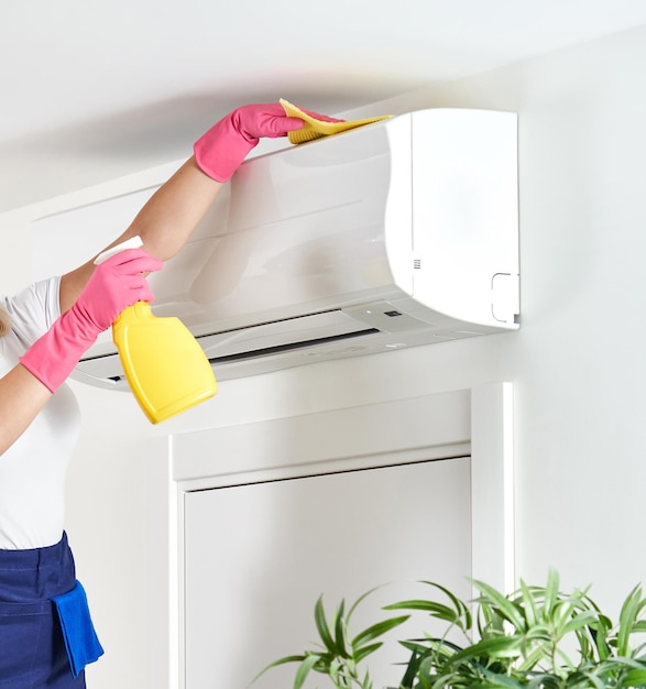 Woman cleaning air conditioner with rag Cleaning service or housewife concept