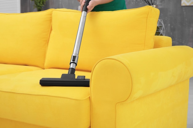 Woman cleaning couch with vacuum cleaner at home