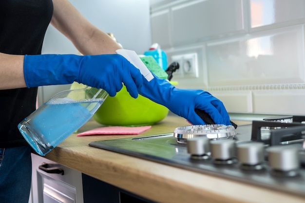 Woman cleaning stainless steel gas surface in the kitchen with rubber gloves.