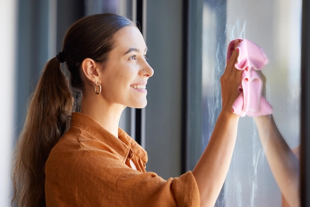 Photo woman cleaning window or wipe glass with a cloth in an apartment home or house and washing bacteria disinfection hygiene and smiling female removing dirt or dust in an office by doing housework