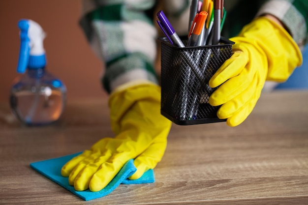 Woman cleans office in the yellow gloves wipes the dust off the office desk