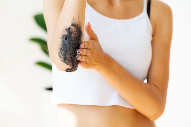 Woman cleans skin of the body with coffee scrub in bathroom