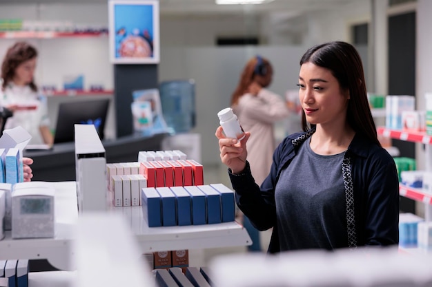 Woman client holding drugs bottle looking at pharmaceutical prescription, buying medication treatment for immune system in pharmacy. Drugstore shelves full with vitamin, supplements ready for purchase