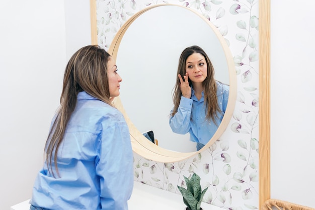 woman in a clinic observes her skin in the mirror after a professional hyaluronic acid application