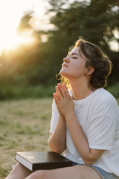 Woman closed her eyes praying in a field during beautiful sunset hands folded in prayer concept for ...