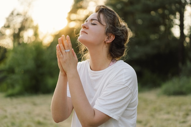 Woman closed her eyes praying in a field during beautiful sunset hands folded in prayer concept for ...