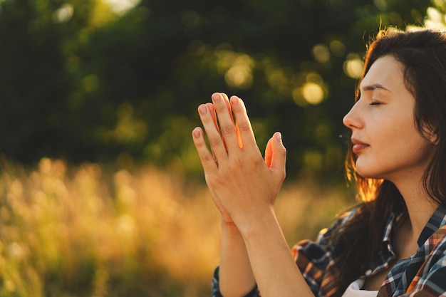 Woman closed her eyes praying in a field during beautiful sunset