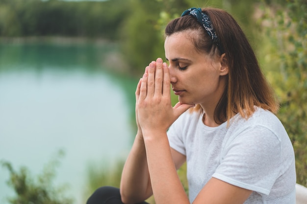 Woman closed her eyes, praying in outdoors. Hands folded in prayer concept for faith, spirituality and religion