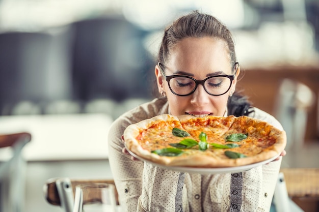 Woman closes her eyes as she enjoys the taste of freshly baked pizza in her hands