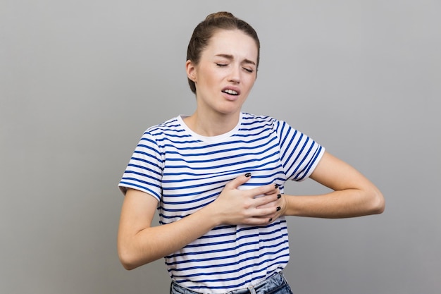 Woman clutching breast and grimacing from painful cramp heart attack at young age cardiac disease