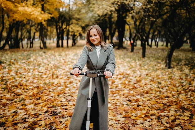 Woman in a coat in autumn on an electric scooter in an autumn park Riding on electric vehicles