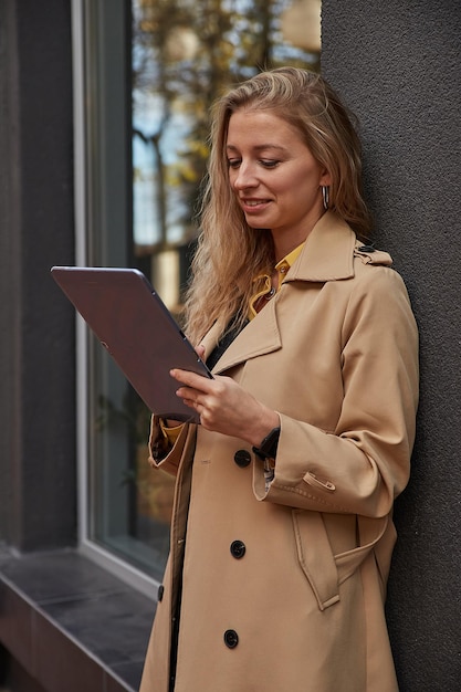 Woman in coat using tablet outdoors on sunny day reading ebook watching movie