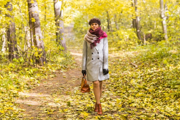 Woman in coat with brown bag standing in autumn park