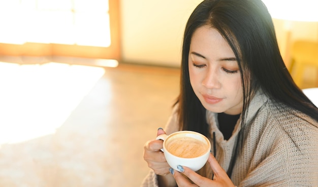 Woman coffee with hand holding a cup in cafe young woman drinking coffee relaxed woman smelling coffee at home in winter with cup coffee