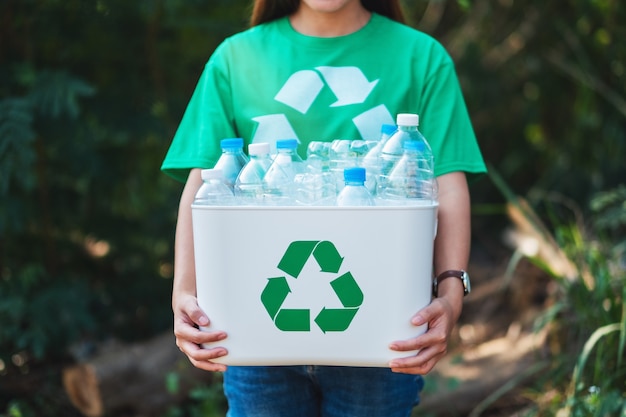 A woman collecting garbage and holding a recycle bin with plastic bottles in the outdoors