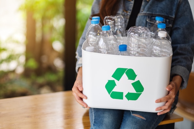 A woman collecting and holding a recyclable garbage plastic bottles into a trash bin at home