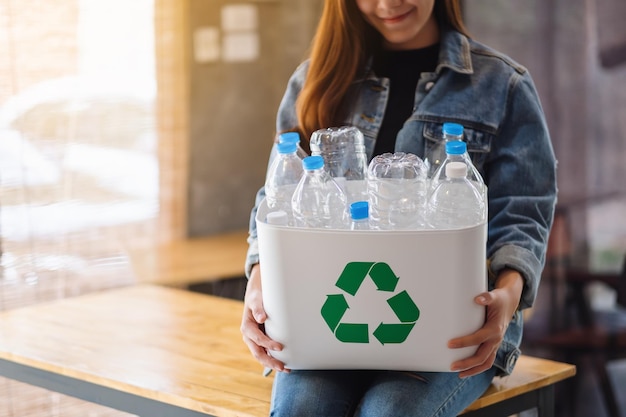 A woman collecting and holding a recyclable garbage plastic bottles in a trash bin at home