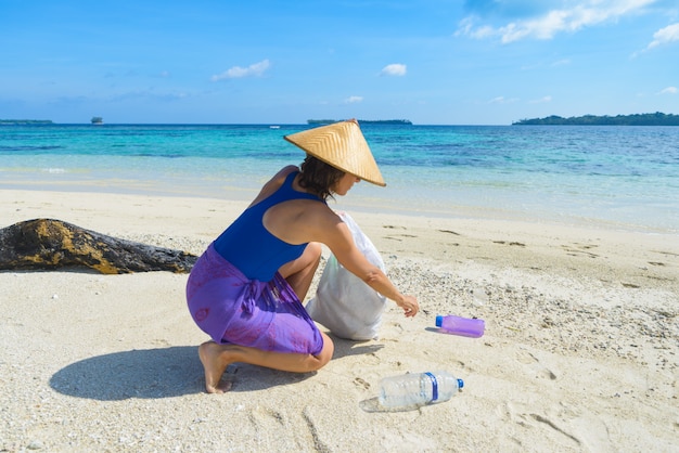 Woman collecting plastic bottles on beautiful tropical beach, recycling concept