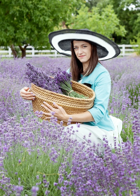 Woman collects lavender in straw basket  Lady in dress and hat in lavender field 