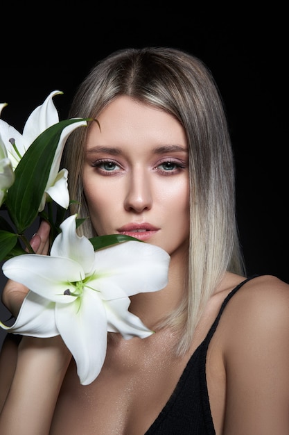 Woman colored hair color of a blonde with lily flower on black background.